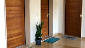 A hallway with three wooden doors, a potted plant, and two doormats. - RESIDENCE VIA LECCE (Merine)