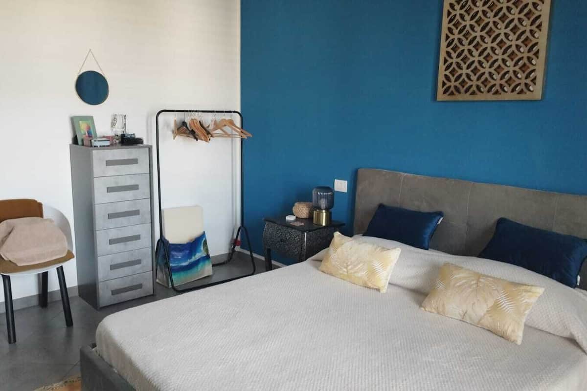 Un dormitorio con cama, una silla, tocador y mesita de noche.
