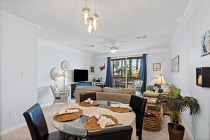 A living room with a dining table set, sofas, a TV, and a ceiling fan. - Gulf-front condo with access to gulf beaches and two community pools. (Dauphin Island)