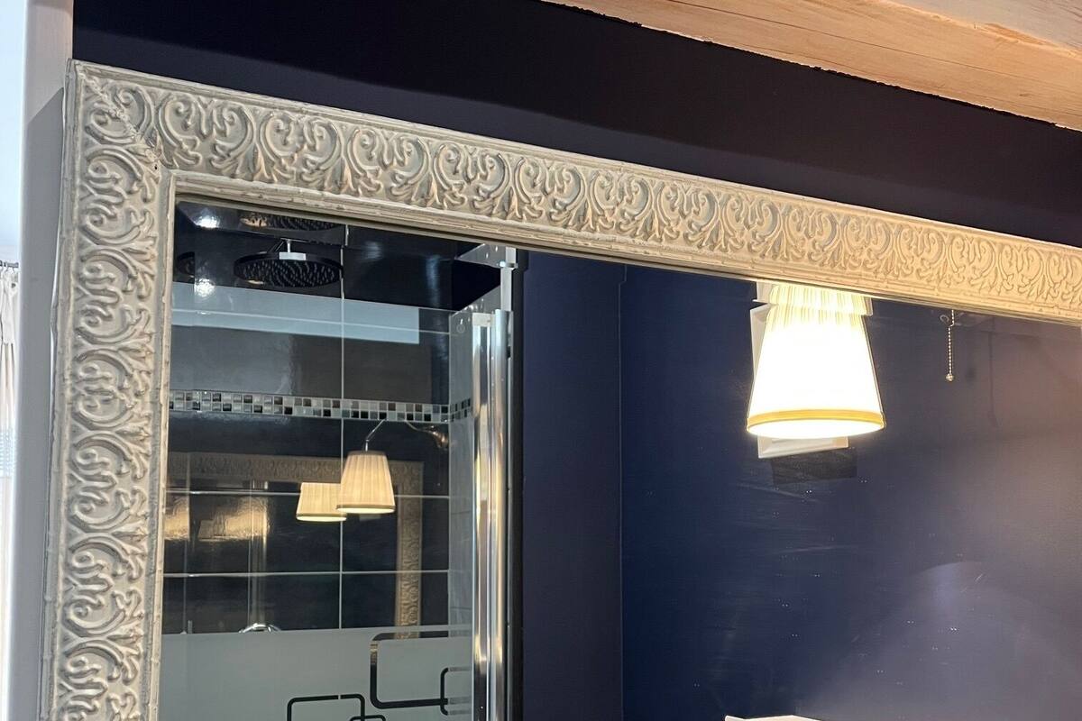 A bathroom with a large mirror, dark walls, and a light fixture.