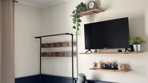 Et værelse med fjernsyn, træhylder, en plante, elkedel og bænk.