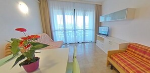 Een woonkamer met een bank, een televisie, een eettafel en een potplant.