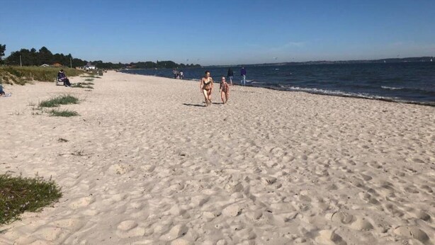 Ein sandiger Strand mit Fußabdrücken, einigen Personen und wolkenlosem Himmel.