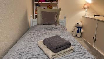 A bedroom with a bed, pillows, a teddy bear, a lamp, and a shelf with toys.