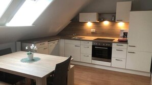 Eine moderne Küche mit Oberlicht, weißen Schränken, einem Einbauofen und einer Essecke mit Tisch und Stühlen.