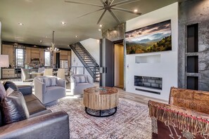 A spacious living area with a fireplace, a round coffee table, and a staircase leading to a kitchen. - Summit Brownstone Retreat with Elevator & Mount LeConte Views (Sevierville)