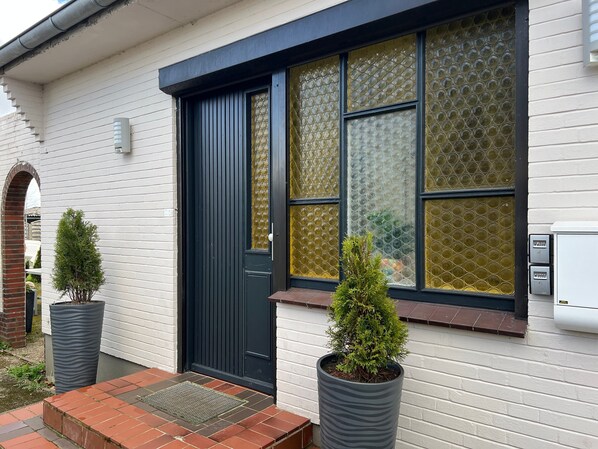 A house with a black door, large windows with bubble patterns, and two potted plants. - Small New Apartment in Jübek with Wi-Fi (Jübek)