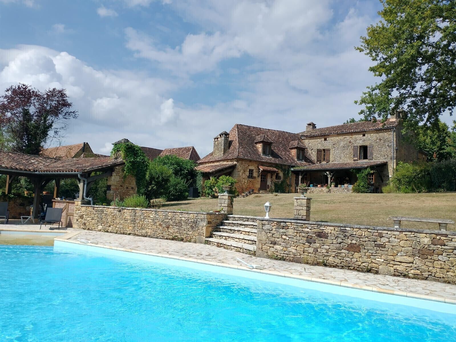 Vista de la piscina y un edificio de piedra con un porche cubierto.