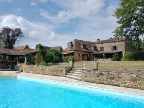 A poolside view of a stone building with a covered patio and a swimming pool. - Charming house with pool for 8 people (Urval)