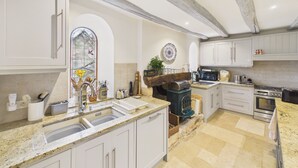 A kitchen with white cabinets, a stone countertop, a wood-burning stove, and a large window with stained glass. - Typical Dordogne house with pool & views (Urval)