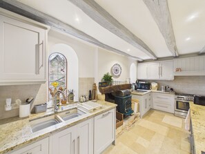 A kitchen with white cabinets, a stone countertop, a wood-burning stove, and a large window with stained glass. - Charming house with pool for 8 people (Urval)