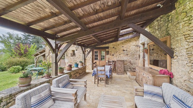 A covered outdoor seating area with stone walls, wooden furniture, and potted plants. - Typical Dordogne house with pool & views (Urval)