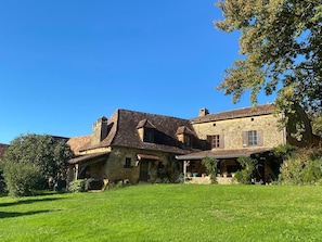 A stone building with a tiled roof, a covered porch, and a grassy lawn. - Charming house with pool for 8 people (Urval)