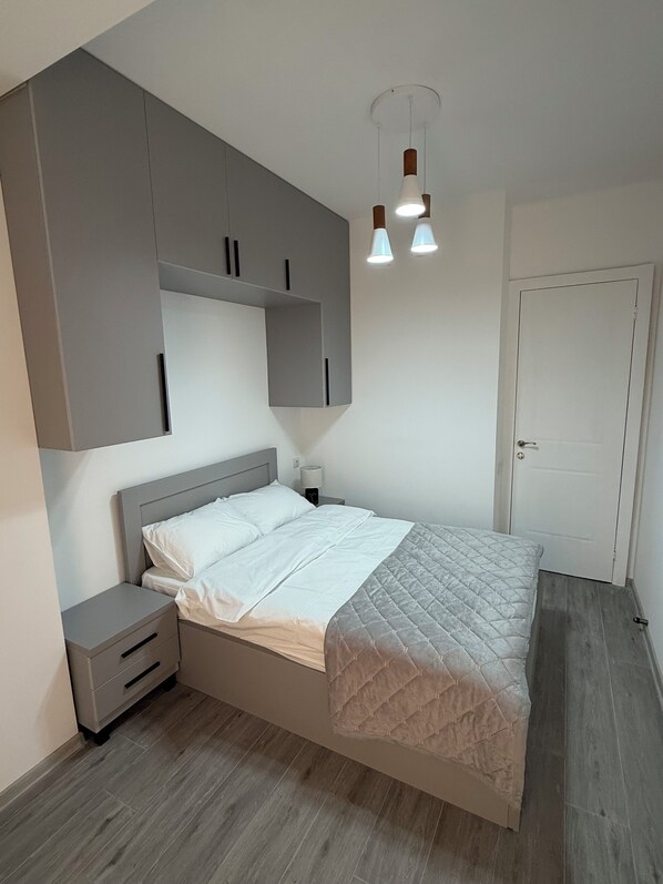 A bedroom with a bed, nightstands, a wardrobe, and pendant lighting.