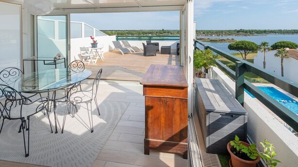 Un balcón con mesa y sillas, vista al mar y una piscina.