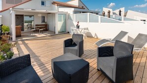 Una terraza en la azotea con mobiliario exterior y un ventanal corredera que da a un espacio interior.