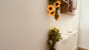 Un couloir avec un mur blanc, une armoire en bois et une plante aux fleurs jaunes.