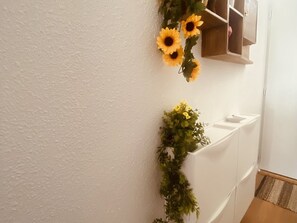 Un couloir avec un mur blanc, une armoire en bois et une plante aux fleurs jaunes.