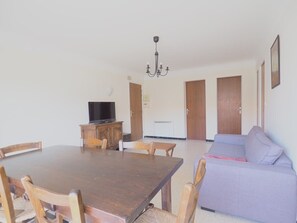 A dining area with a wooden table and chairs, a television on a cabinet, a sofa, and a chandelier. - Charming city center apartment - 6 guests (Le Grau-du-Roi)