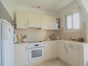 A kitchen with white cabinets, a built-in oven, a microwave, and a window. - Charming city center apartment - 6 guests (Le Grau-du-Roi)