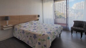 Una camera da letto con un letto, comodino, lampada, sedia e vista panoramica tramite una porta vetrata.