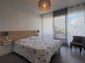 Ein Schlafzimmer mit Bett, Nachttisch, Lampe, Stuhl und Blick durch eine Glastür.