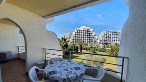 Un balcone con tavolo e sedie, vista su edifici moderni e cielo sereno.