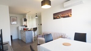 Una camera moderna e luminosa con un tavolo da pranzo, sedie, un laptop e una zona cucina sullo sfondo.