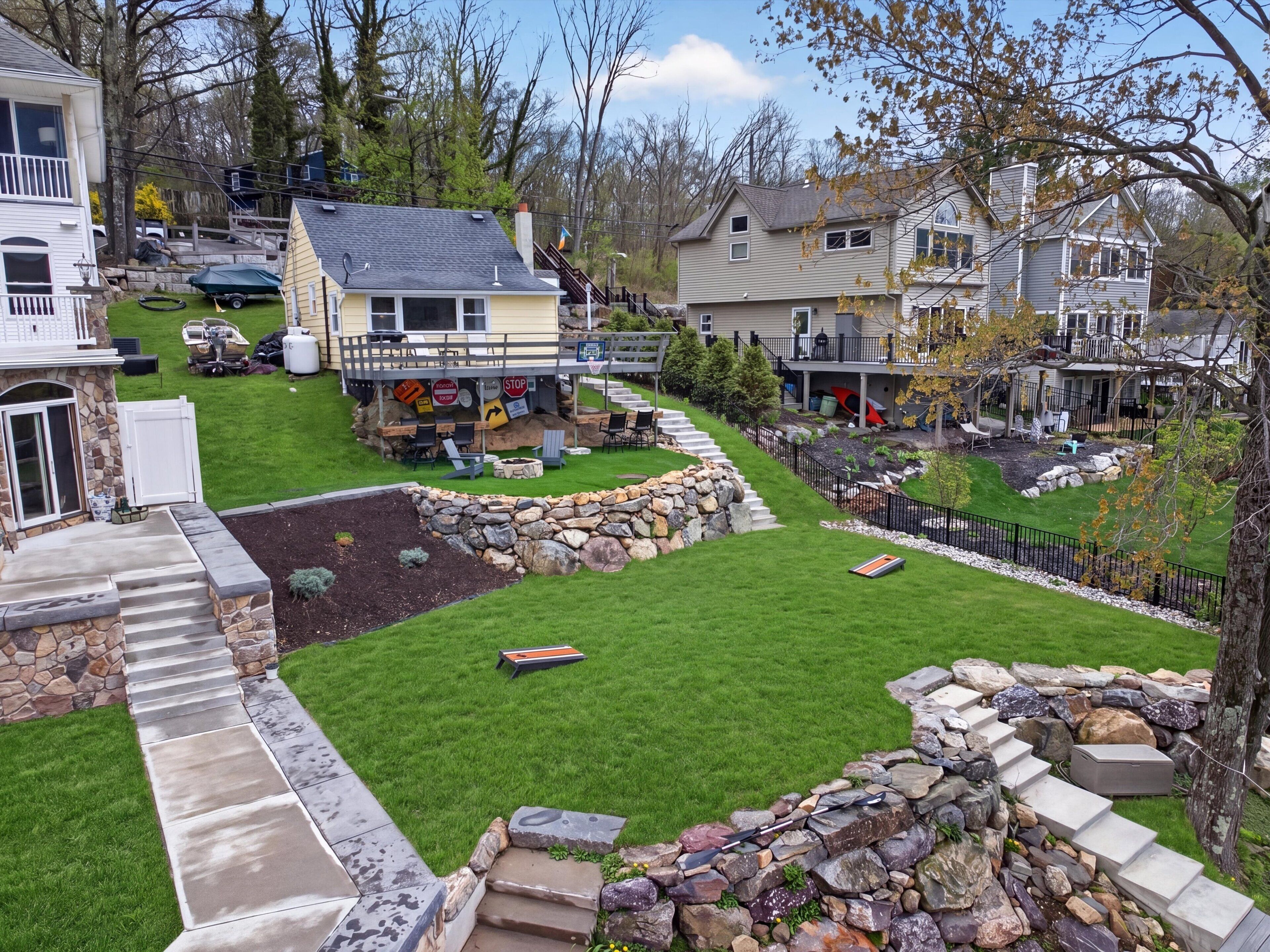 A residential area with a well-maintained lawn, stone steps leading to a porch, and a small deck area with outdoor furniture.