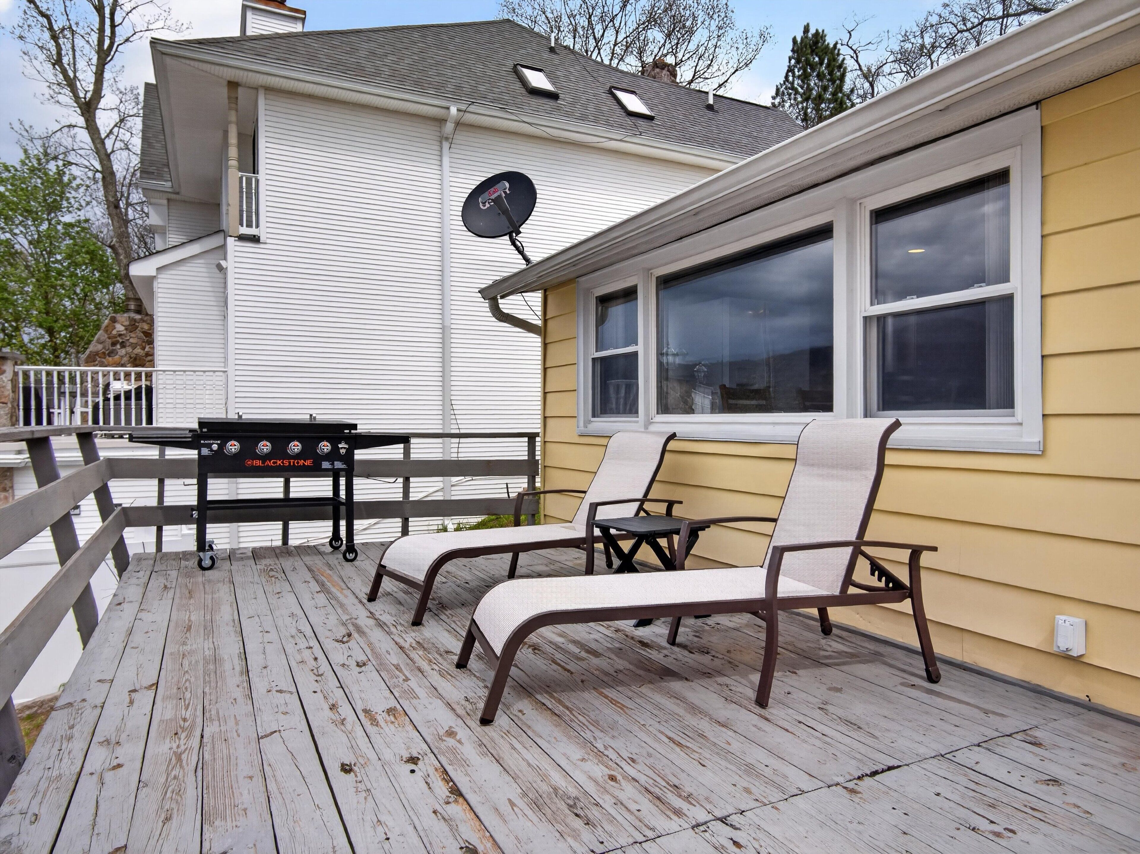 A deck with a grill, two chairs, and a window.