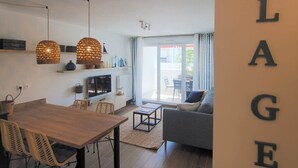 A modern living room with a sofa, a dining table with chairs, and a kitchen area with a TV. - Apartment, AC, parking - 4 guests (Le Grau-du-Roi)