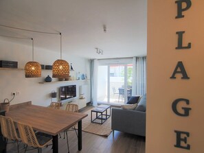 A modern living room with a sofa, a dining table with chairs, and a kitchen area with a TV. - Apartment, AC, parking - 4 guests (Le Grau-du-Roi)