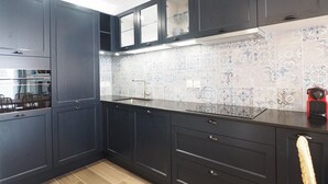 A modern kitchen with dark cabinetry, a patterned backsplash, and a wooden floor. - Apartment, AC, parking - 4 guests (Le Grau-du-Roi)