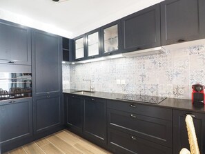 A modern kitchen with dark cabinetry, a patterned backsplash, and a wooden floor. - Apartment, AC, parking - 4 guests (Le Grau-du-Roi)