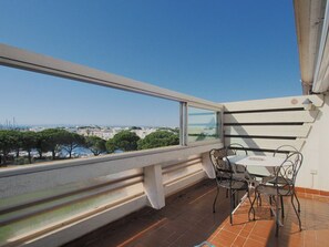 A balcony with a table and chairs, overlooking a marina and cityscape. - Charming studio, terrace, parking - 4 guests (Le Grau-du-Roi)