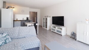 Un apartamento moderno con kitchenette, comedor, sala de estar con televisor y dormitorio con colcha estampada.
