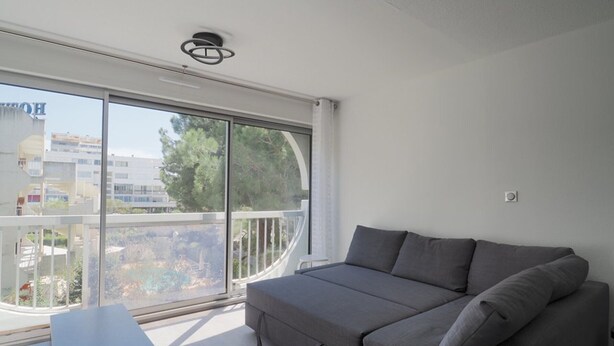 Un balcón con sofá, una mesa y vista a edificios y árboles.