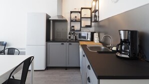 Cocina compacta con microondas, cafetera y un reloj en la pared.