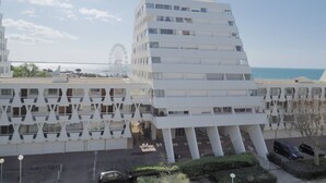 Ein modernes Gebäude mit markantem, winkelförmigem Design, das mehrere Balkone und einen Parkplatz vor der Fassade aufweist.