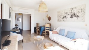 Ein Wohnzimmer mit einer Couch, einem Fernseher, einem Essbereich mit Stühlen und einem großen Wandbild.