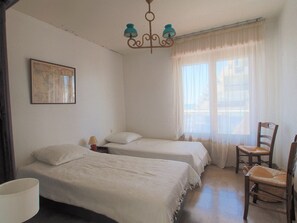 A room with two beds, a chair, a lamp, and a window with curtains. - Sea view apartment, AC, parking - 6 guests (La Grande-Motte)