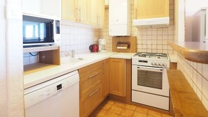 Kompakti keittiö, jossa on puukaapit, mikroaaltouuni, kahvinkeitin, astianpesukone ja liesi.