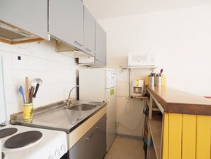 Een kleine keuken met een spoelbak, fornuis, magnetron en een geel aanrecht.