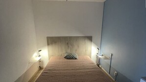 Makuuhuoneessa on puinen sängynpääty, raidallinen päiväpeite, kaksi yöpöytälamppua ja yöpöytä, jossa on lamppu.