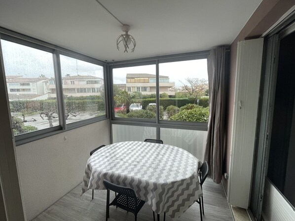 A balcony with a table and chairs, large windows, and a view of buildings and greenery. - Renovated apartment with parking - 7 guests (Le Grau-du-Roi)