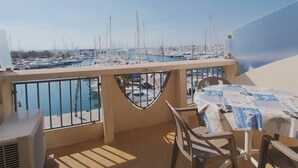A balcony with a view of a marina, a table with a tablecloth, and a chair. - Apartment with AC, sea view, parking - 4 guests (La Grande-Motte)