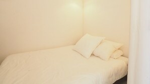 A minimalist bedroom with a single bed, a hanging light fixture, and a plain wall. - Apartment with AC, sea view, parking - 4 guests (La Grande-Motte)