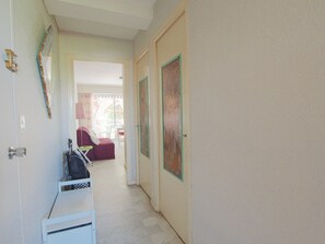 Ein Flur mit einer weißen Bank, einer Tür mit grünem Rahmen und Blick in einen Raum mit einem roten Sessel und einem Tisch.
