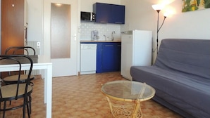 Ett kompakt bostadsutrymme med ett litet kök, en matplats med stolar, en soffa och ett soffbord i glas.