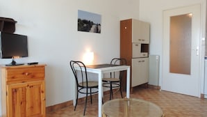 Ett litet pentry med ett vitt bord, två stolar, ett träskåp, en tv och en tavla på väggen.